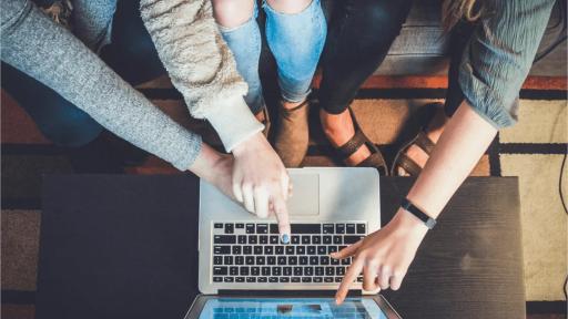 Three people sitting on a couch pointing at a laptop.